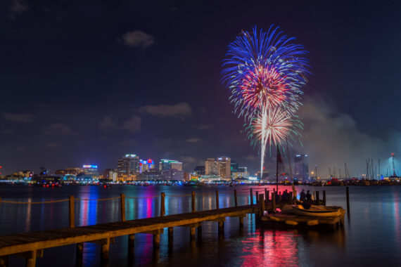 Fireworks seen over a bay with a dock and a city in the background