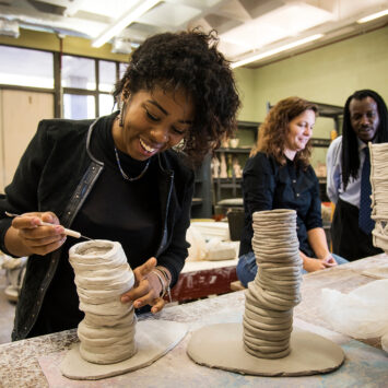 Two female students workin on pottery with an black male instructor looking on